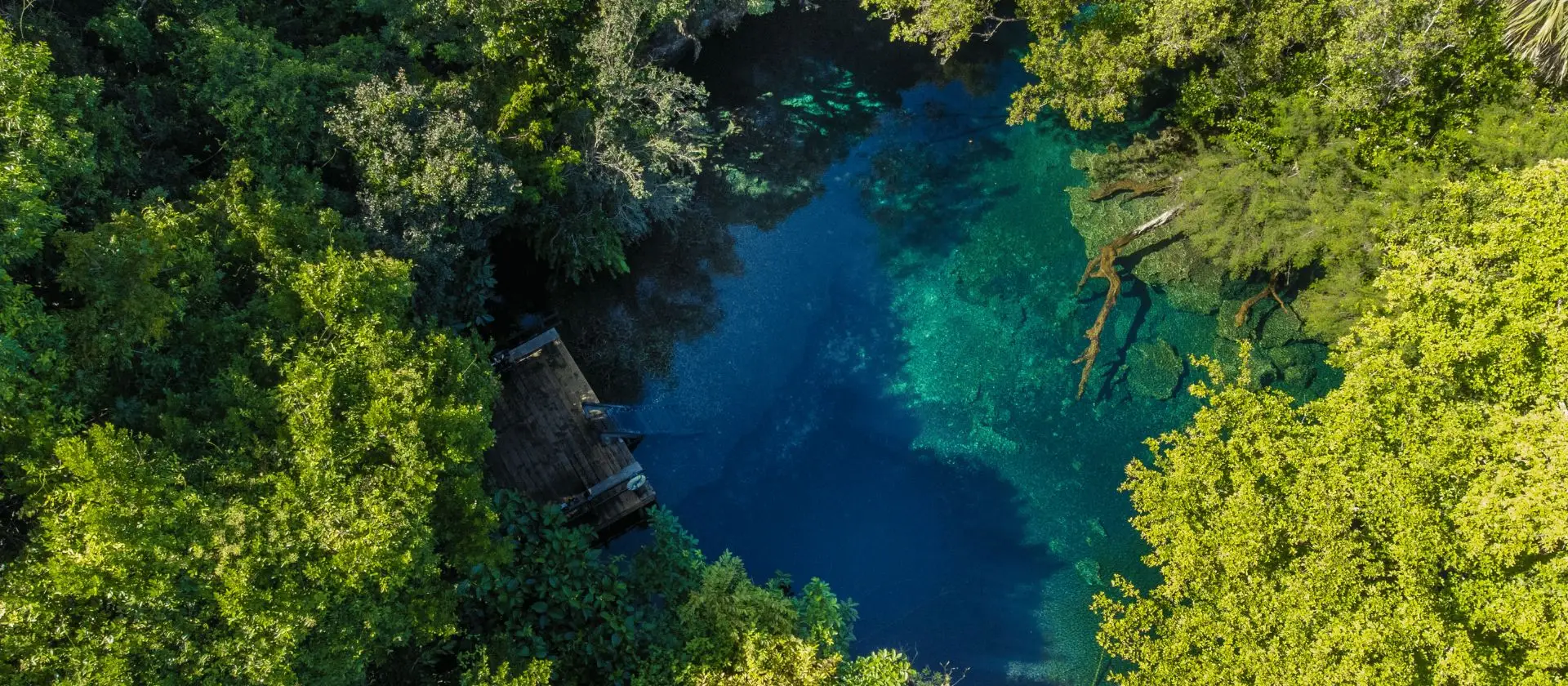 Vista aérea de laguna azul con muelle de madera en Ojos Indígenas, Punta Cana