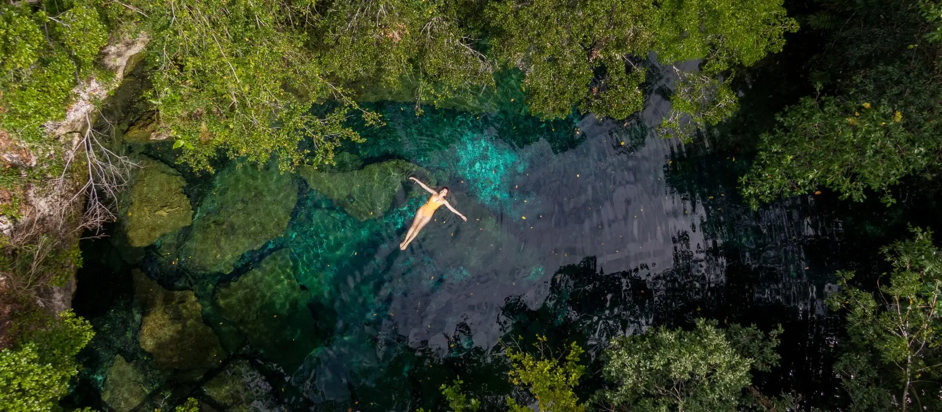 Vista aérea de mujer flotando en laguna cristalina de la Reserva Ojos Indígenas